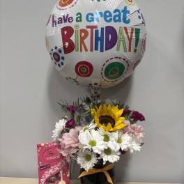 Birthday balloon above a mixed flower bouquet with chocolates in a vase