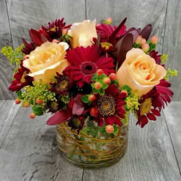 Low arrangement of peach roses and dark red gerbera daisies in a clear glass vase