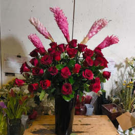 Tall arrangement of red roses with pink spiked tropical flowers in a glossy black vase