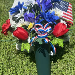 Red, white, and blue floral arrangement in a green vase with an American flag ribbon