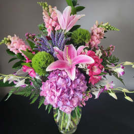 Pink lilies and hydrangea in a glass vase with purple spikes
