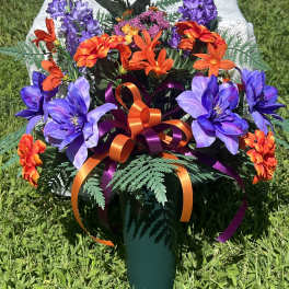 Artificial bouquet of purple and orange flowers in a green vase with ribbon