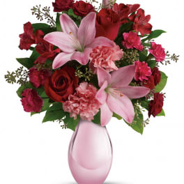 Pink lilies, red roses, and carnations in a pink glass vase