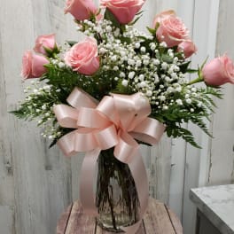Pink roses in a glass vase with white baby's breath and a pink ribbon