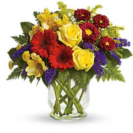 Mixed bouquet of yellow roses, red daisies, and purple filler in a glass vase