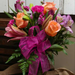 Bouquet of orange roses, pink lilies, and purple flowers with a magenta ribbon