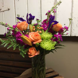 Colorful bouquet of orange roses, purple irises, and green chrysanthemums in a glass vase