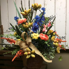Colorful mixed flower arrangement in a woven basket with a burlap ribbon