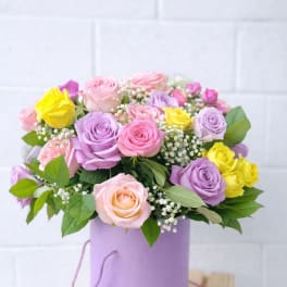 Pastel pink, lavender, and yellow roses with baby’s breath in a lavender hatbox container