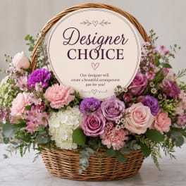 Basket arrangement of pink and purple flowers with a designer choice sign