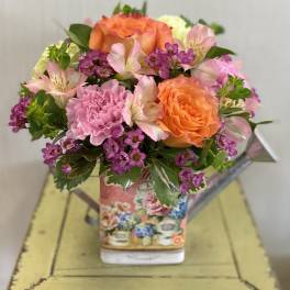 Bouquet of orange roses, pink carnations, and purple filler flowers in a decorative vase