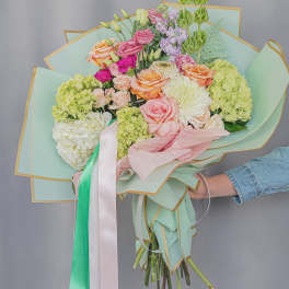 Handheld bouquet of pastel roses, hydrangeas, and chrysanthemums wrapped in mint paper