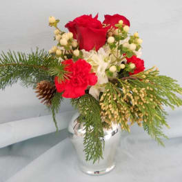 Red roses and white flowers in a clear glass vase with pine greenery