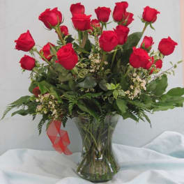 Red roses arranged in a clear glass vase with greenery
