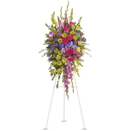 Tall standing floral spray with pink, purple, and yellow flowers on a white easel