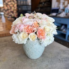Pastel roses and white blooms arranged in a light blue vase
