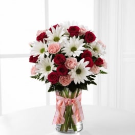 Bouquet of red roses, pink carnations, and white daisies in a glass vase
