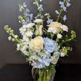White roses and blue flowers arranged in a glass vase