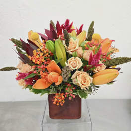 Mixed bouquet of peach roses, orange lilies, and pink accents in a square vase
