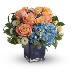 Peach roses and blue hydrangeas in a square glass vase