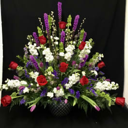 Large floral arrangement with red roses, white blooms, and purple spikes in a black basket