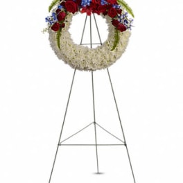 Standing wreath of white flowers with red roses and blue blooms on a metal easel
