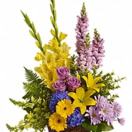 Tall mixed arrangement with yellow lilies, snapdragons, purple roses and daisies in a wicker basket