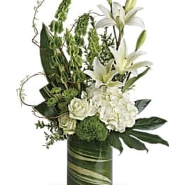 Tall white and green floral arrangement with lilies in a leaf-wrapped glass vase