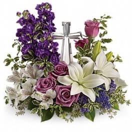 Sympathy arrangement of white lilies and lavender roses with a silver cross centerpiece