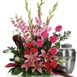 Pink lilies, roses, and red carnations arranged beside a silver cremation urn