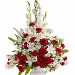 Tall red and white arrangement with roses, carnations, lilies and snapdragons in a white pedestal vase