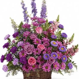 Tall basket arrangement of pink roses, purple daisies, asters, and delphinium in mixed lavender tones