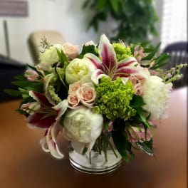 Bouquet of white lilies, pale roses, and green hydrangea in a glass vase