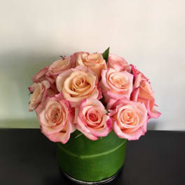 Pink and peach roses arranged in a green round box