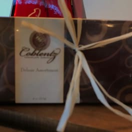 Wrapped gift box with a white ribbon and a red bottle behind it