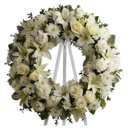 White floral wreath on a stand with roses, lilies, and daisies