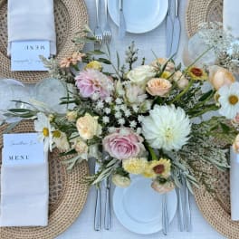 Pastel floral centerpiece on a set dining table with white plates and woven chargers