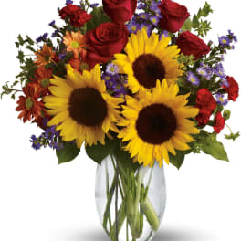 Bouquet of sunflowers, red roses, and purple daisies in a glass vase
