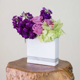 Purple and pink roses with green orchids in a white vase