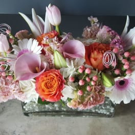 Pink and white floral arrangement with orange roses in a glass vase