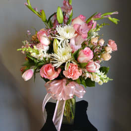 Pink and white mixed bouquet in a clear glass vase with a pink ribbon