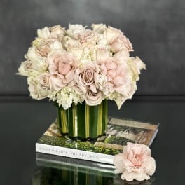 Low arrangement of blush and ivory roses in a leaf-lined glass vase on stacked books