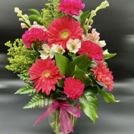 Bright pink gerbera daisies, carnations, and light alstroemeria in a clear vase with pink bow
