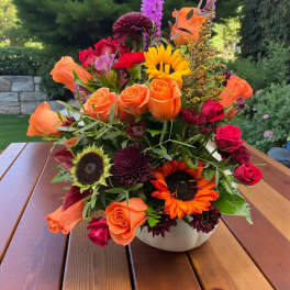 Mixed bouquet of orange and red flowers in a white bowl vase