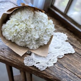 White hydrangea bouquet wrapped in brown paper on a wooden table