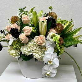 Mixed floral arrangement with pale roses, white orchids, and lilies in a white vase
