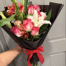 Bouquet of pink roses and white lilies wrapped in black paper with a red ribbon