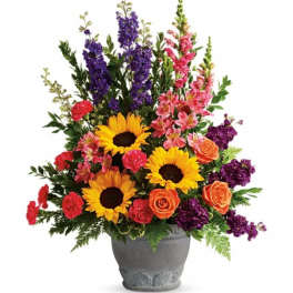 Colorful mixed bouquet in a gray vase with sunflowers, roses, and tall purple blooms