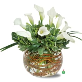 White calla lilies in a round glass vase with woven brown accents