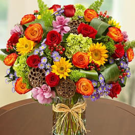 Colorful mixed flower bouquet in a glass vase with a raffia bow